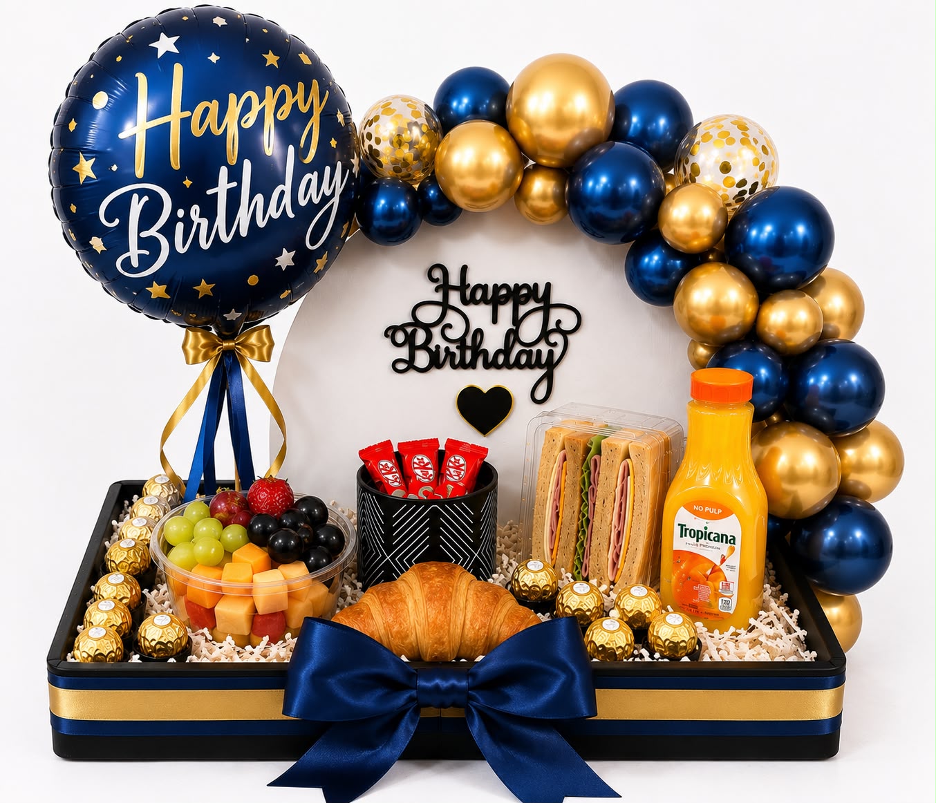 Bandeja de desayuno sorpresa con globo Happy Birthday azul, arco de globos azules y dorados, frutas y croissant