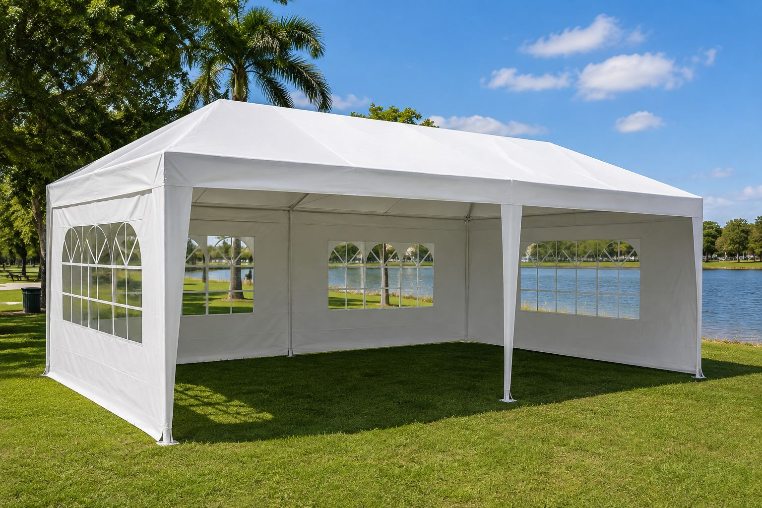 Carpa 10x20 blanca con paredes laterales con ventanas montada en área verde junto a un lago